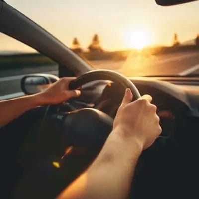 Hände am Lenkrad in einem Auto bei untergehender Sonne